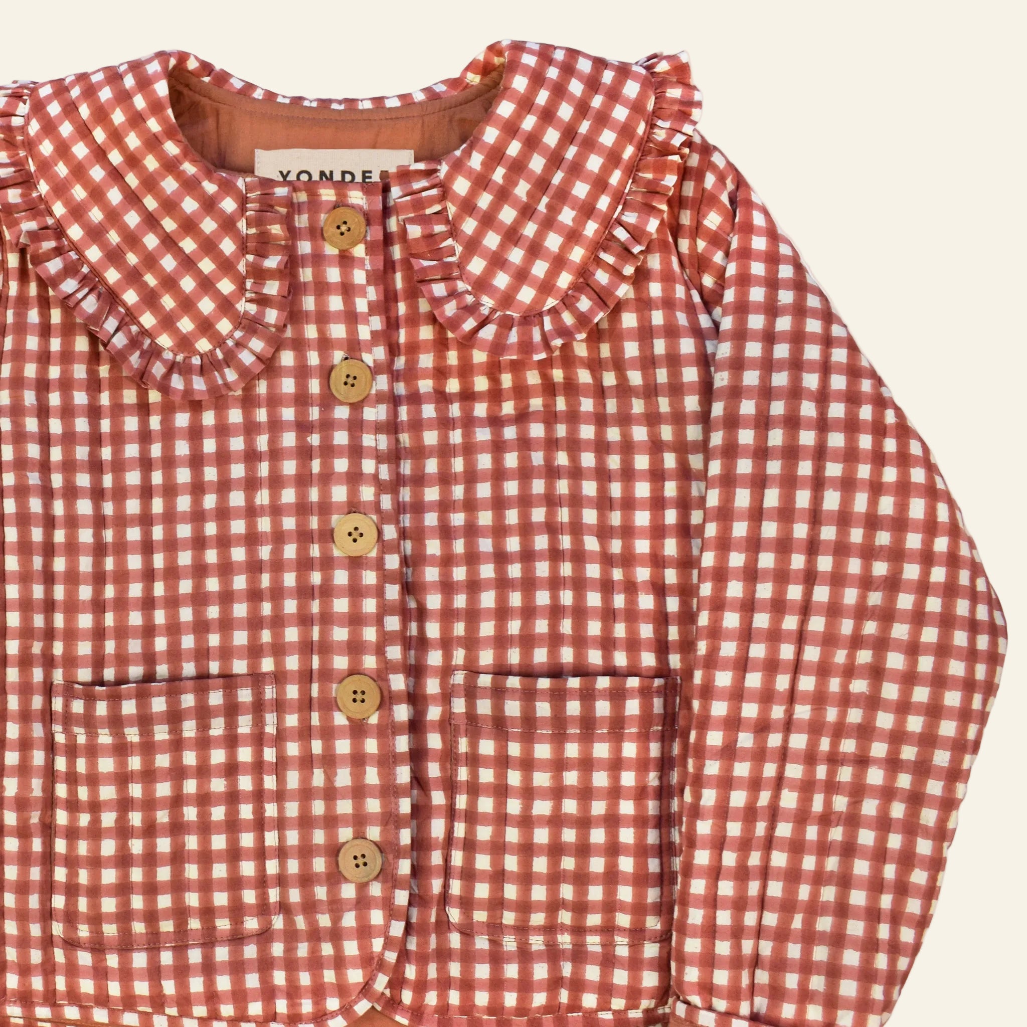 Closeup of cotton quilted jacket printed with red gingham pattern and frill collar