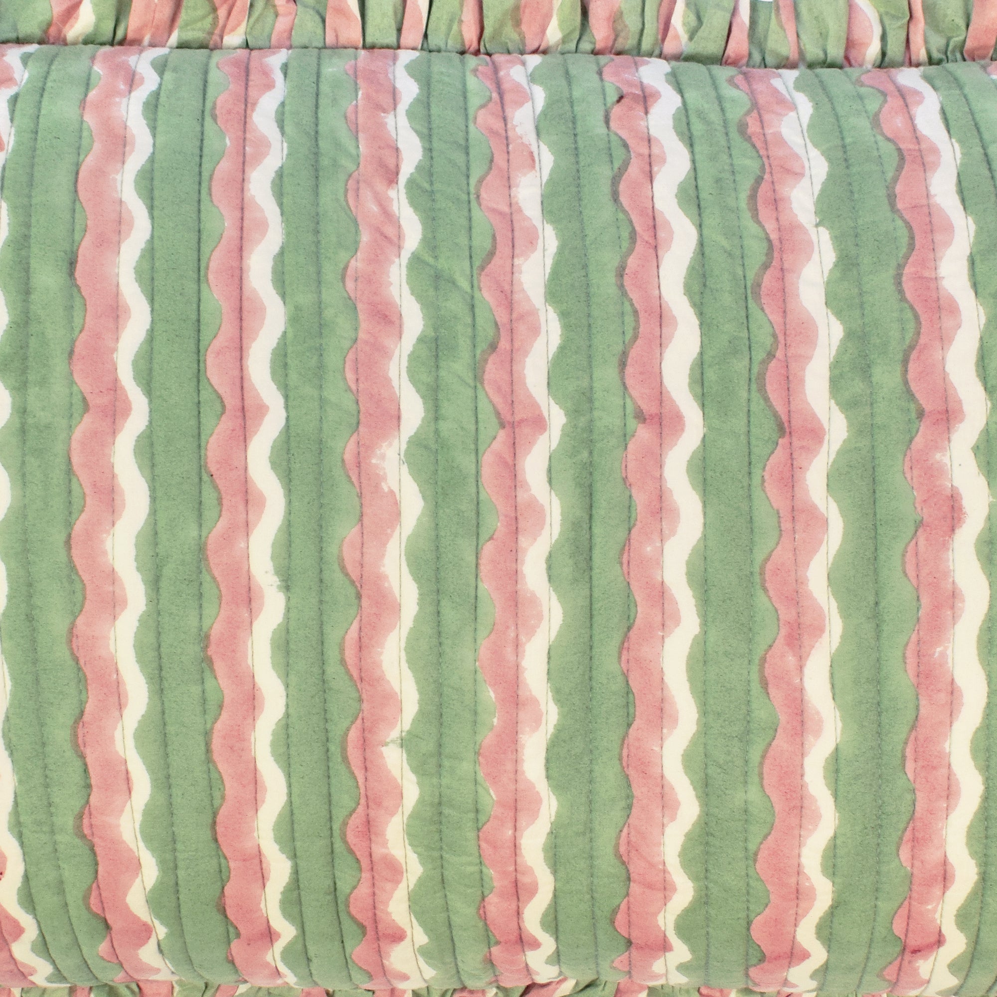 Closeup of long cotton quilted cushion printed with green and pink striped wave pattern and frill border