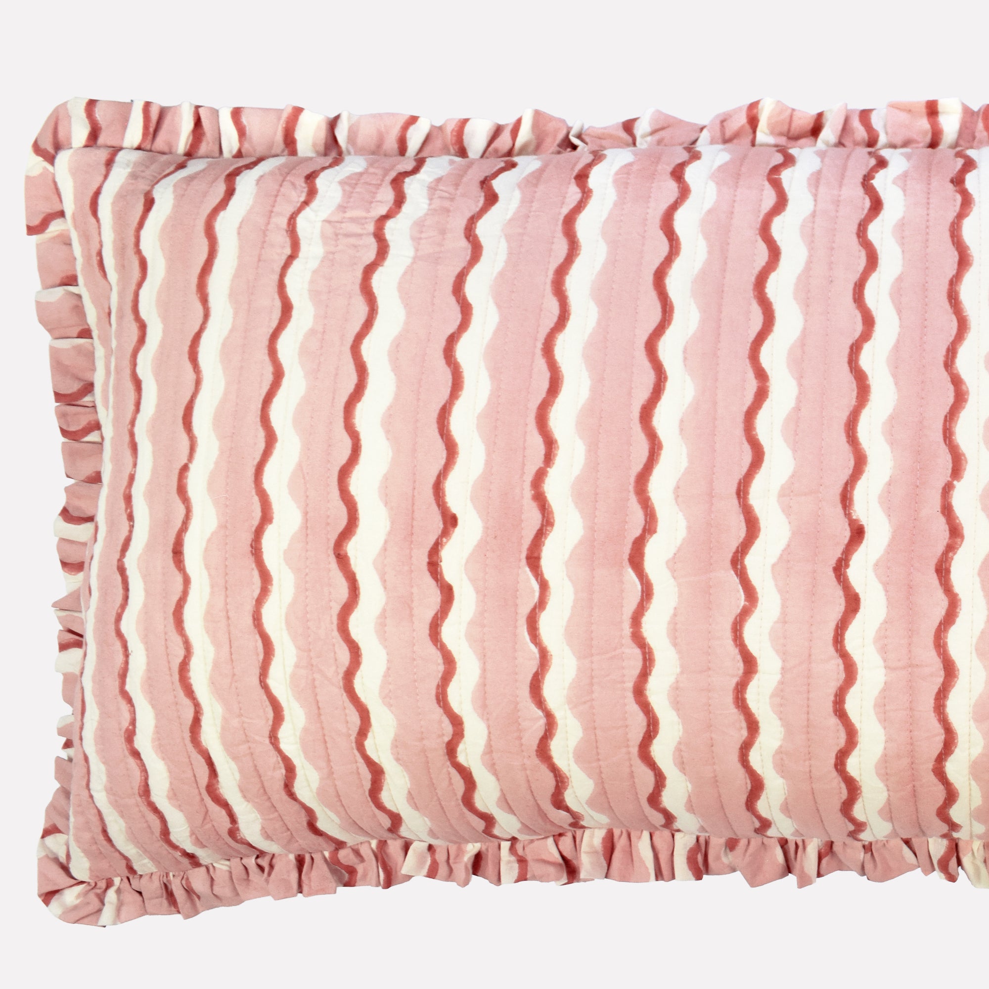 Closeup of long cotton quilted cushion printed with pink and white striped wave pattern and frill border