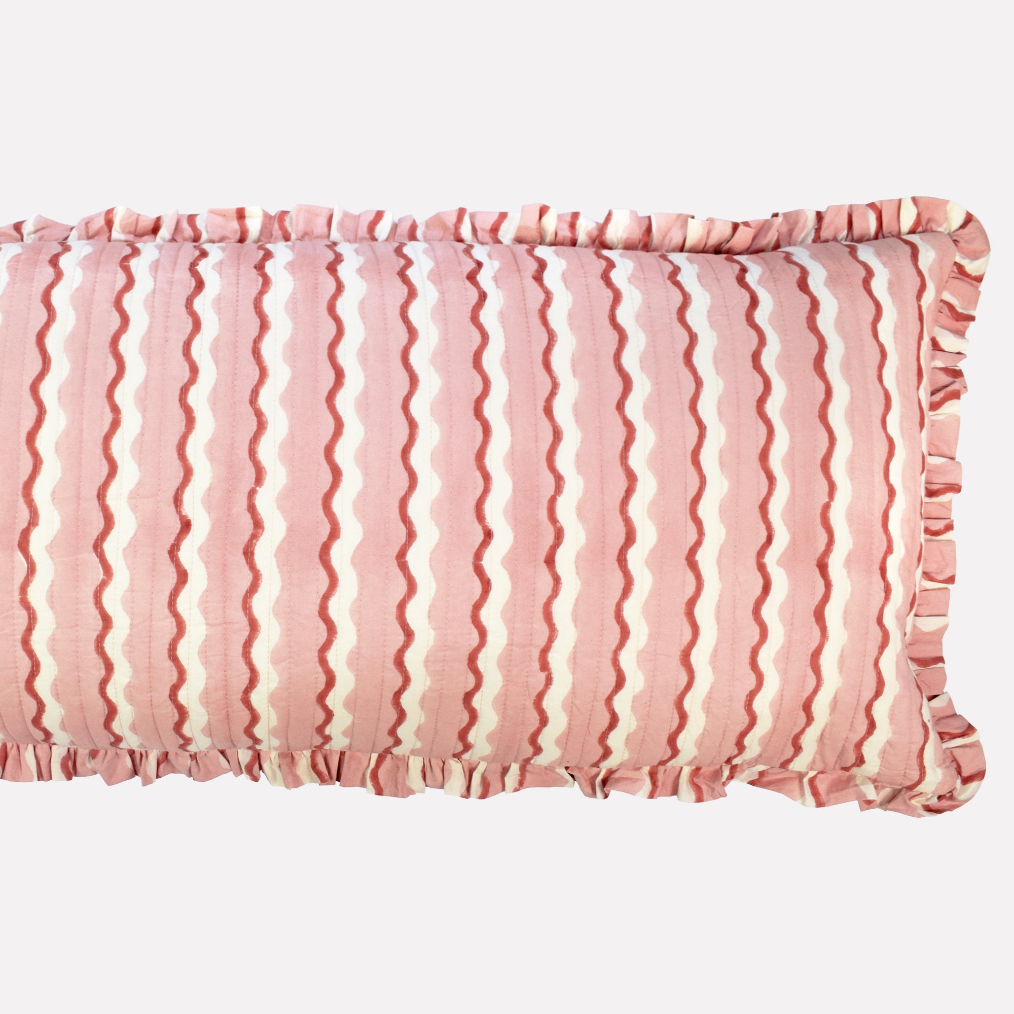 Closeup of long cotton quilted cushion printed with pink and white striped wave pattern and frill border