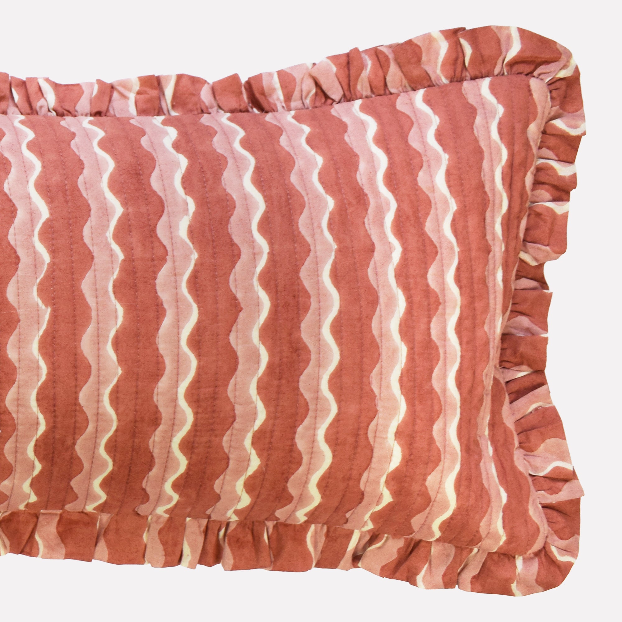Closeup of long cotton quilted cushion printed with pink striped wave pattern and frill border