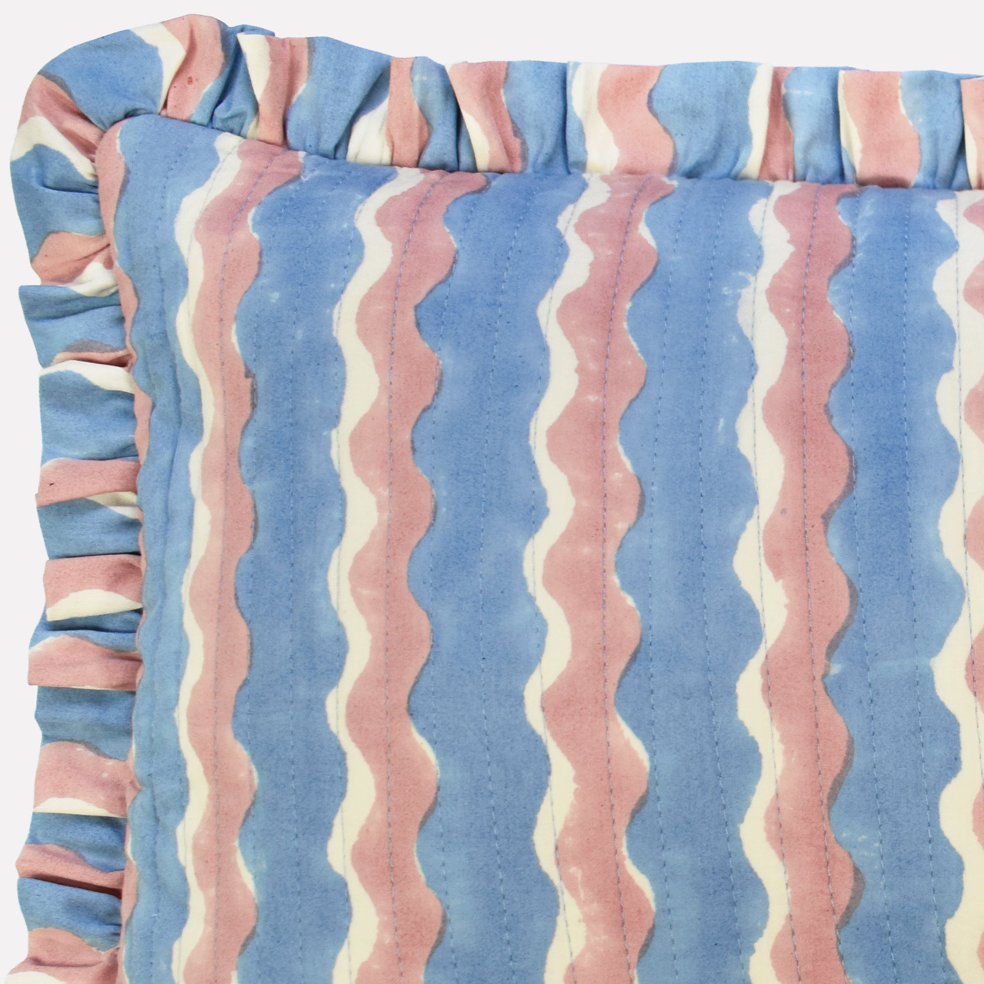 Closeup of cotton quilted cushion printed with blue and pink striped wave pattern and frill border