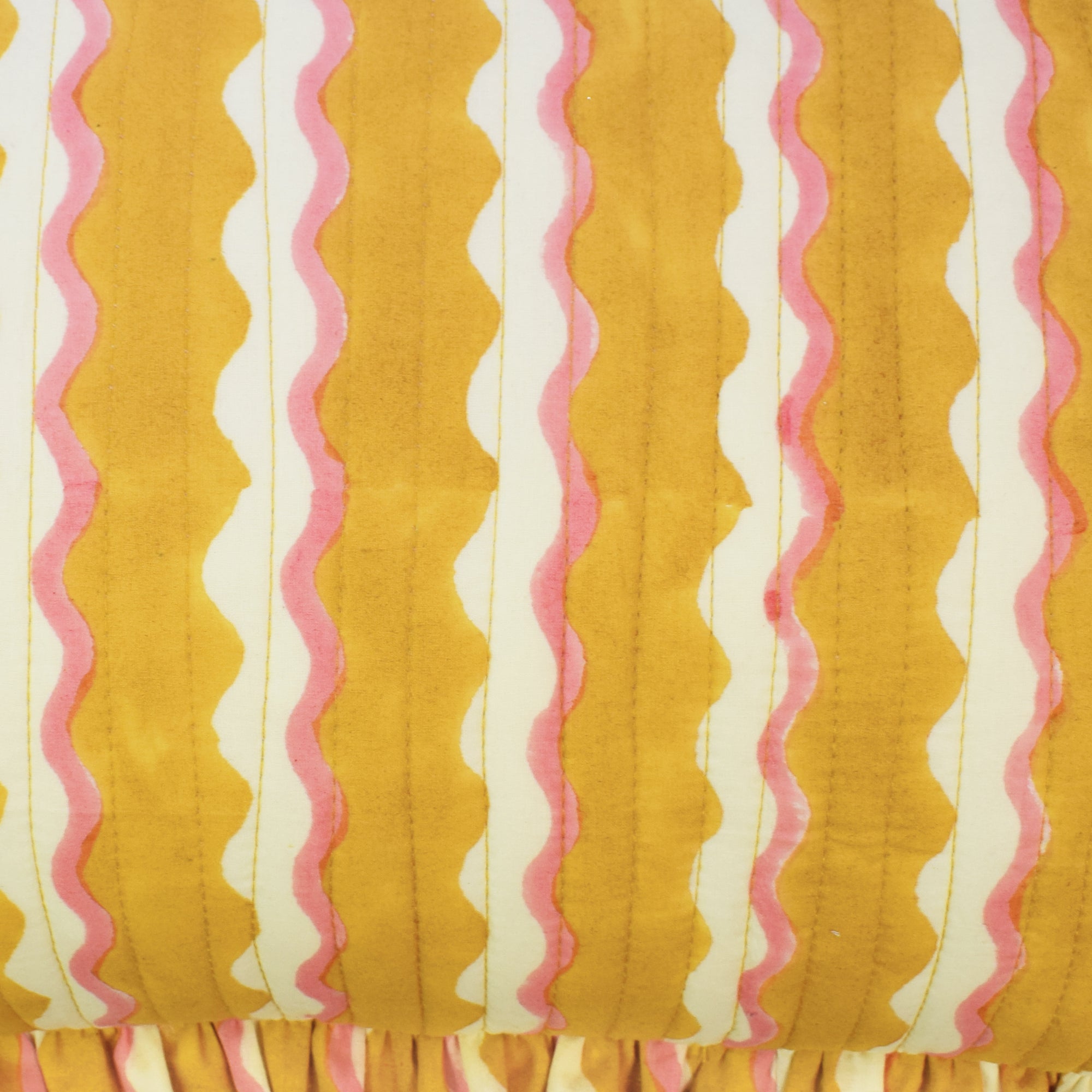 Closeup of small cotton quilted cushion printed with yellow and white striped wave pattern and frill border