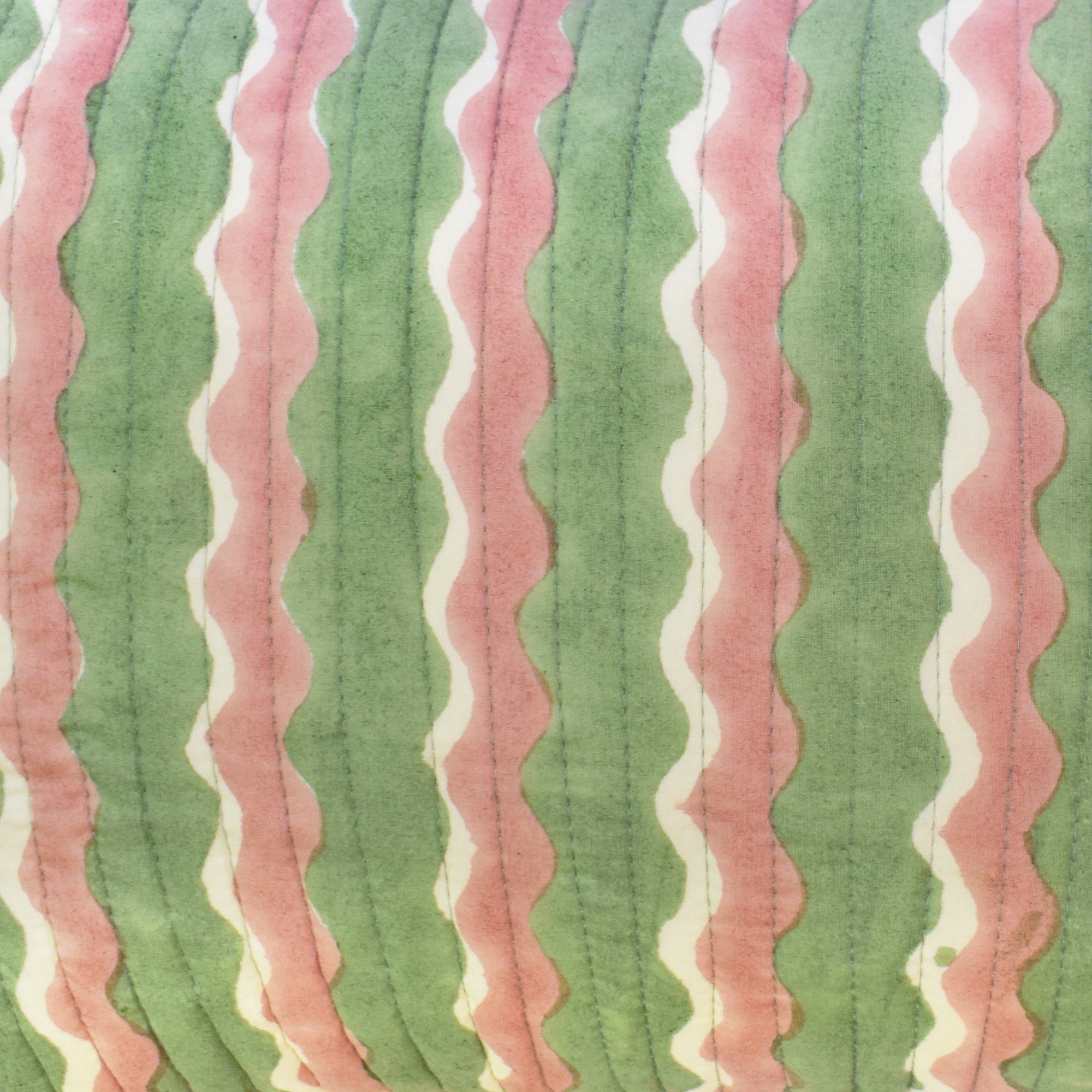 Closeup of small cotton quilted cushion printed with green and pink striped wave pattern and frill border