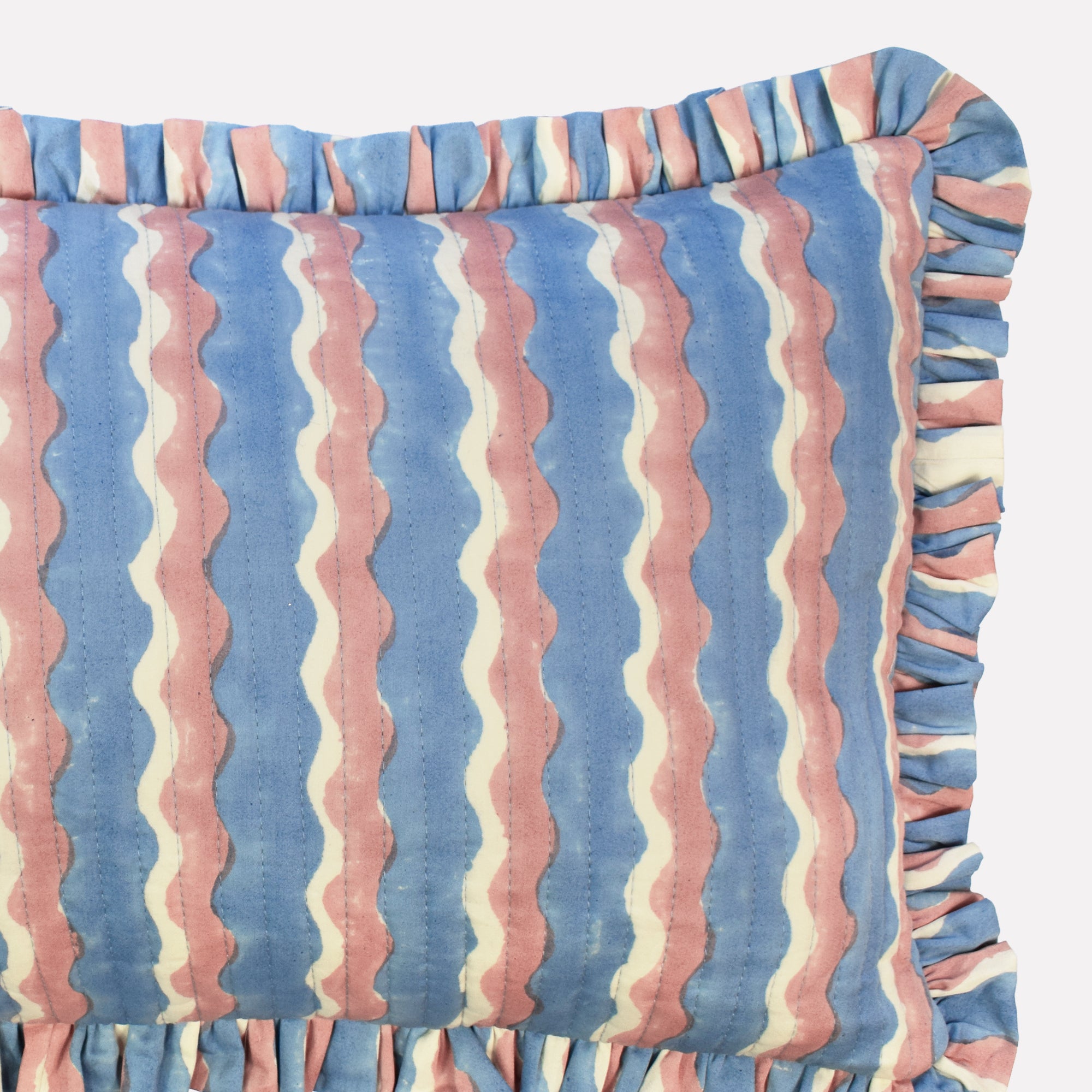 Closeup of small cotton quilted cushion printed with blue and pink striped wave pattern and frill border