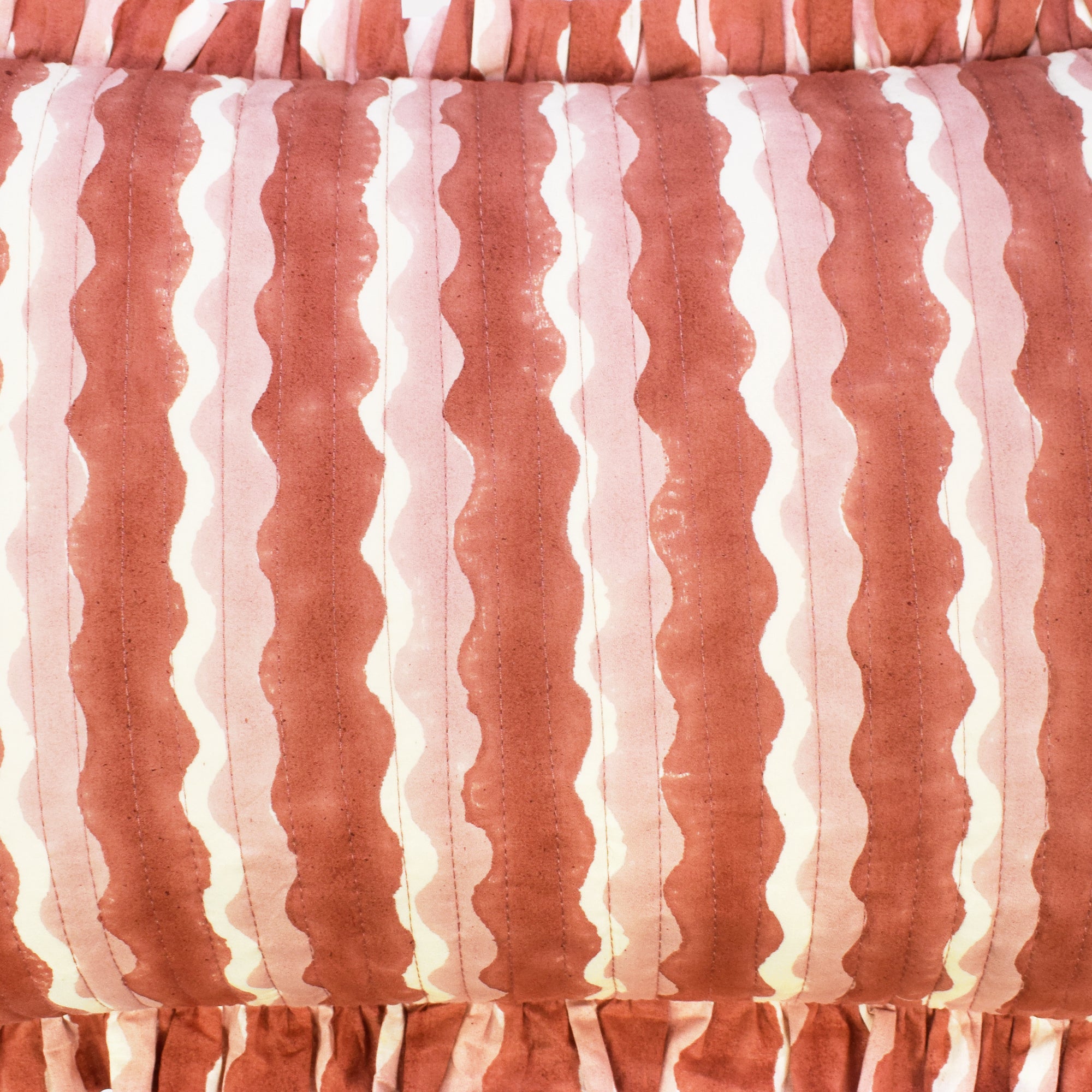 Closeup of small cotton quilted cushion printed with pink striped wave pattern and frill border