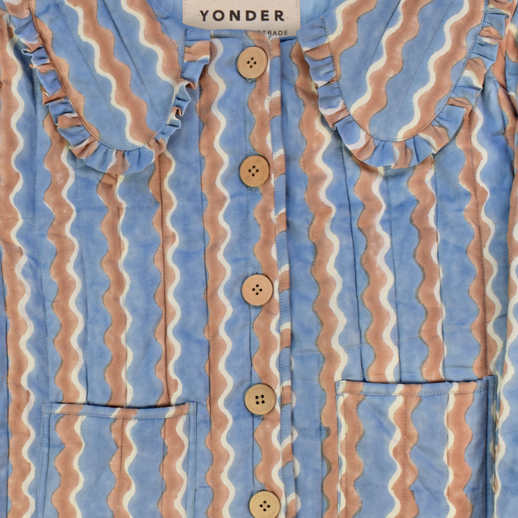 Closeup of cotton quilted jacket printed with blue and brown striped wave pattern and frill collar