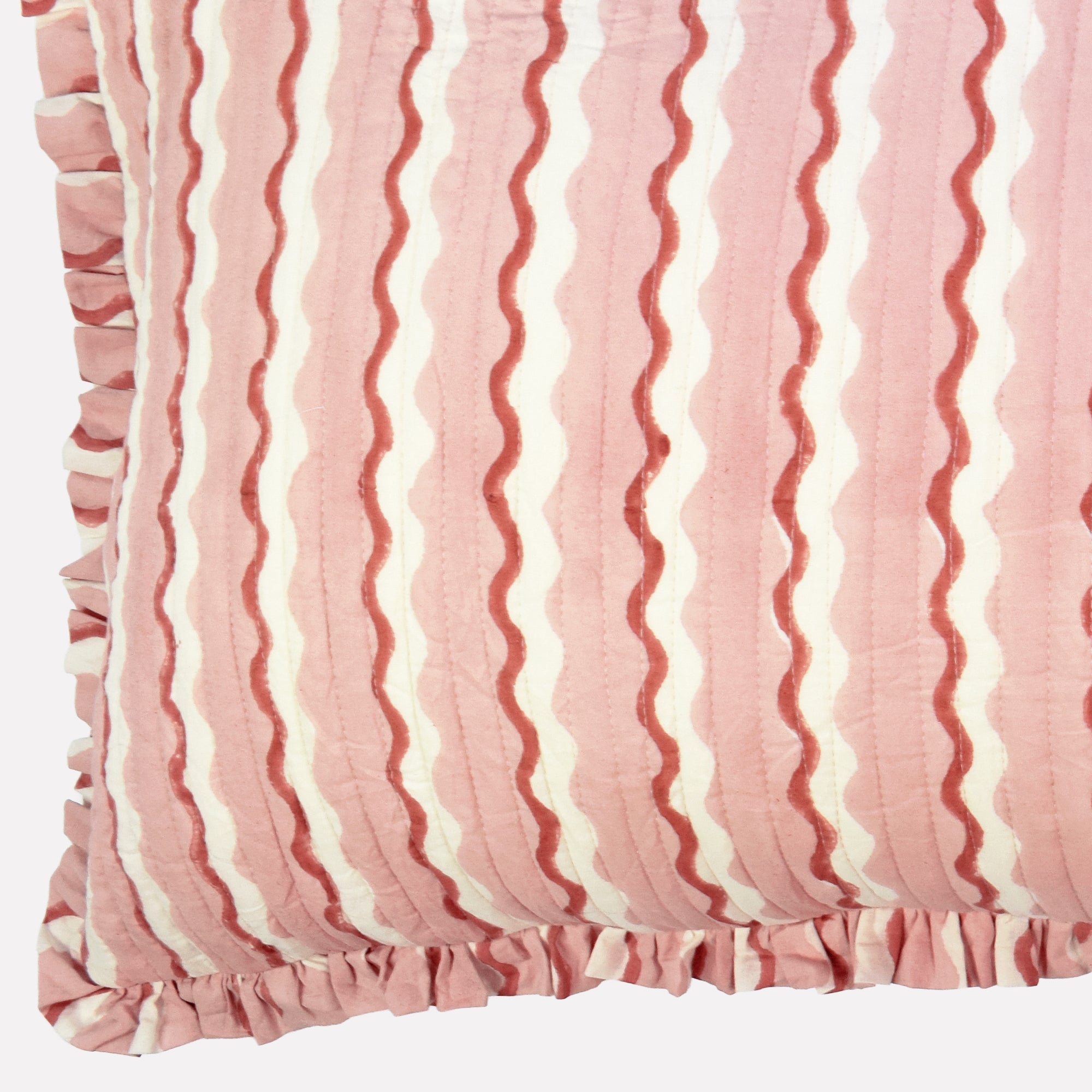 Closeup of long cotton quilted cushion printed with pink and white striped wave pattern and frill border