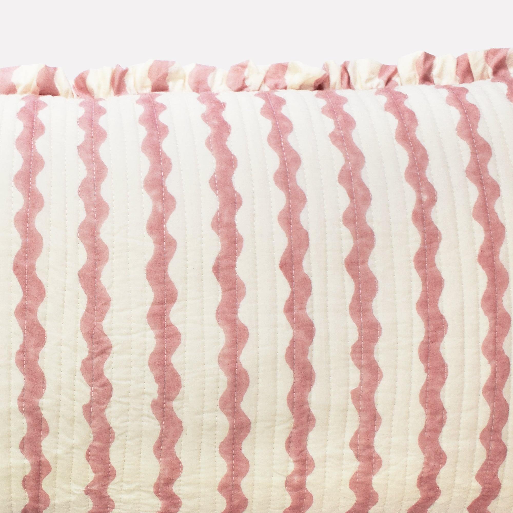 Closeup of long cotton quilted cushion printed with pink and white striped wave pattern and frill border