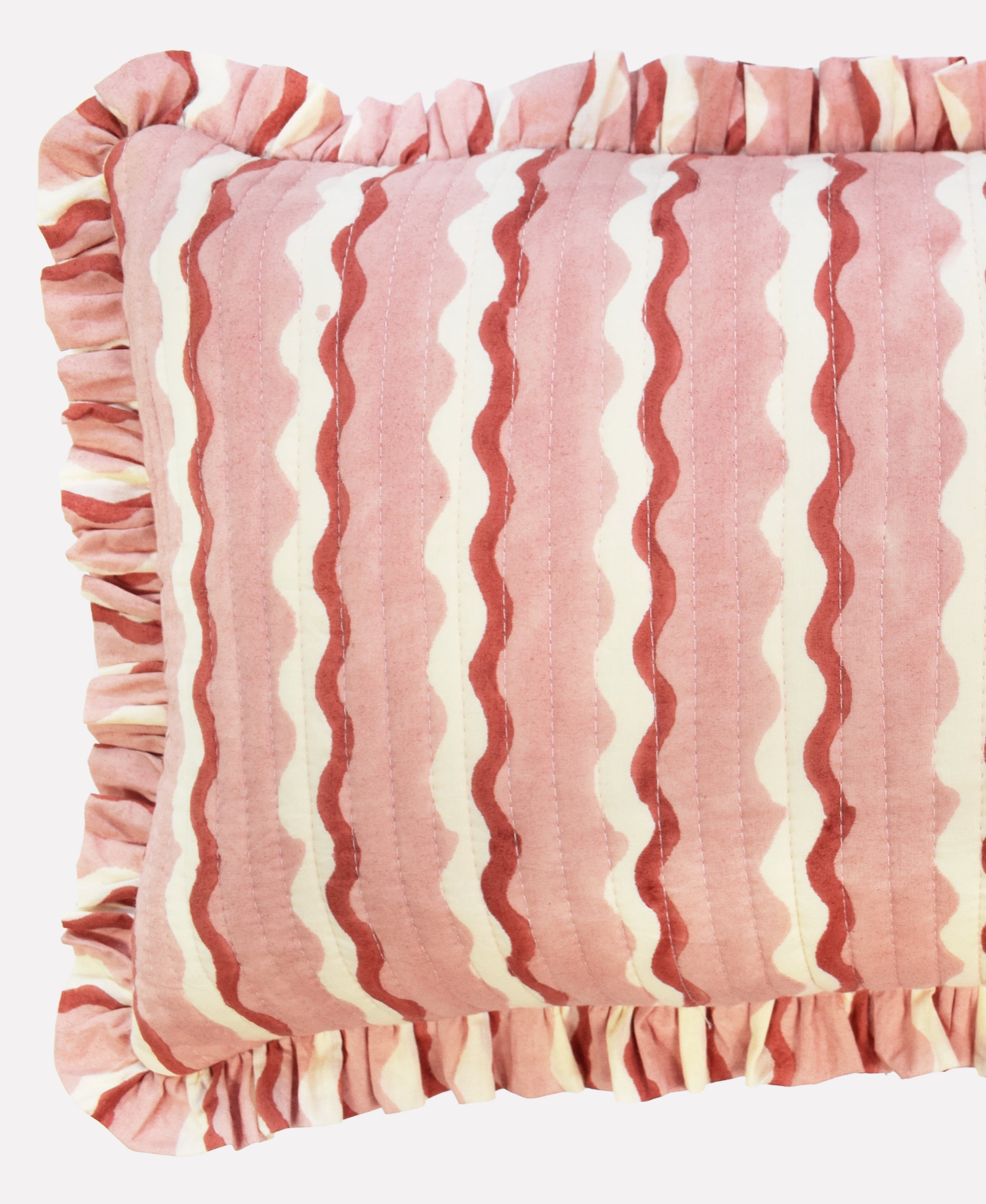 Closeup of small cotton quilted cushion printed with pink and white striped wave pattern and frill border