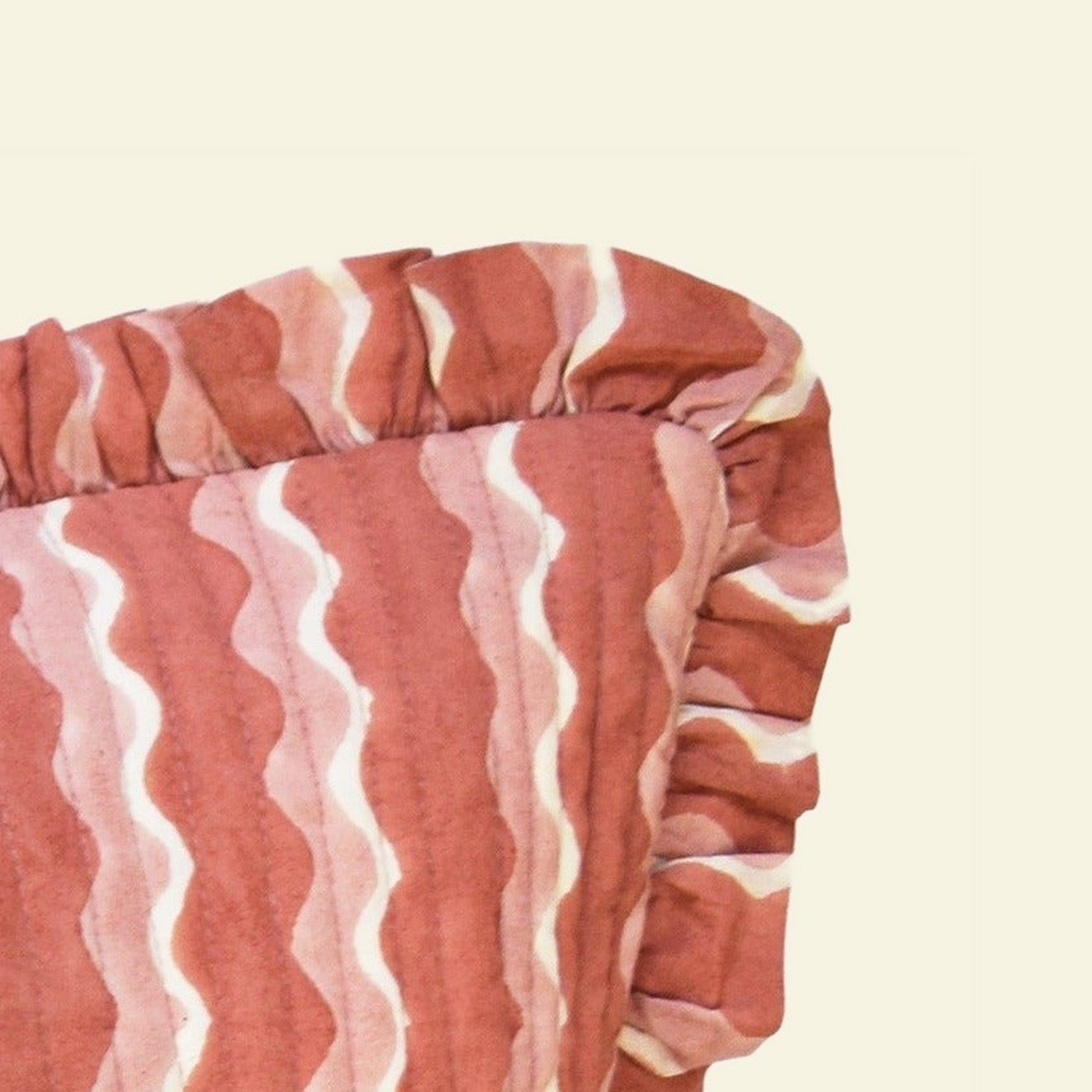 Close-up of Yonder Living Whirly ginger bolster quilted frill cushion, warm ginger block-printed wave and frilled edge